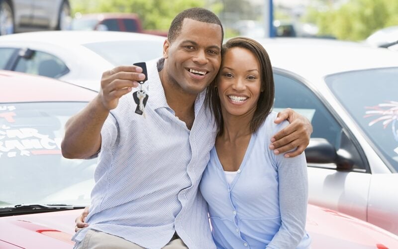 Couple sitting on hood of used car holding the keys
