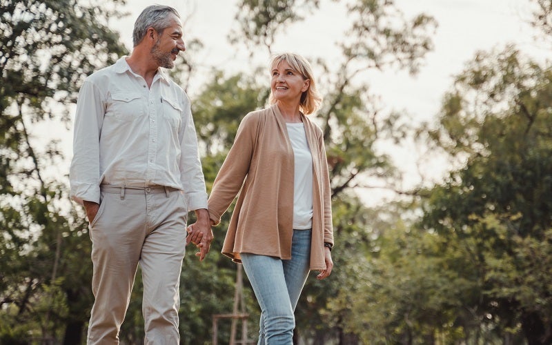 Elderly couple holding hands and walking through a park